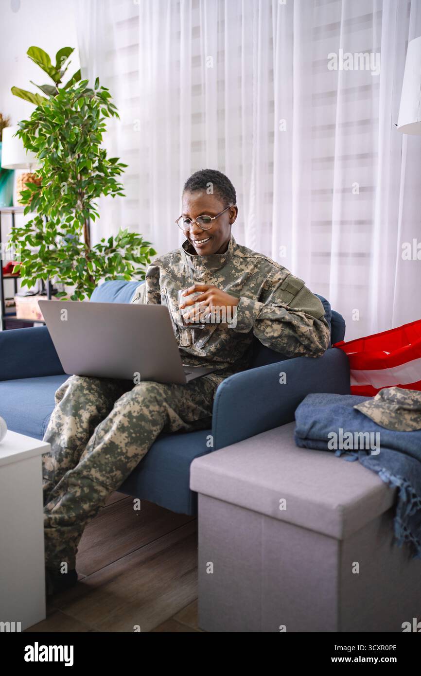 Soldat afro-américain souriant à l'aide d'un ordinateur portable à la maison Banque D'Images
