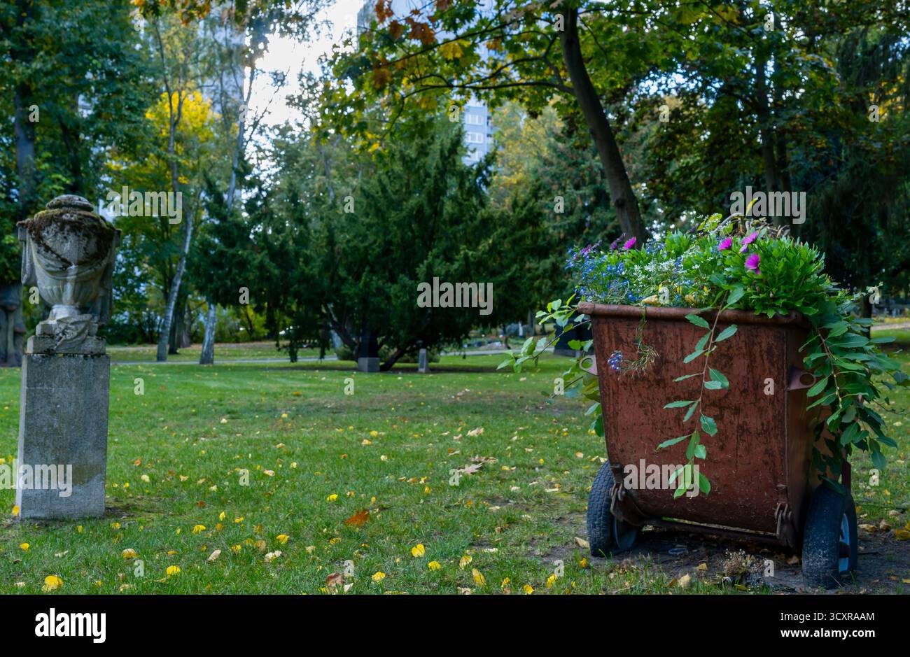 Vieille brouette en métal remplie de fleurs colorées debout sur Georgen paroissiale Friedhof I à Berlin Prenzlauer Berg, Allemagne. Banque D'Images