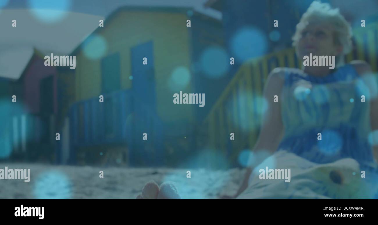 Femme mature assise portant une robe rayée bleue sur la plage de sable près des cabines, espace de copie Banque D'Images