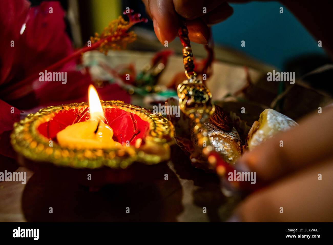 Une main plane gracieusement au-dessus d'une diya incandescente, tenant un rakhi délicat ou un ornement, une offrande d'amour, de protection et de révérence. Banque D'Images Une main plane gracieusement au-dessus d'une diya incandescente, tenant un rakhi délicat ou un ornement, une offrande d'amour, de protection et de révérence. Banque D'Images
