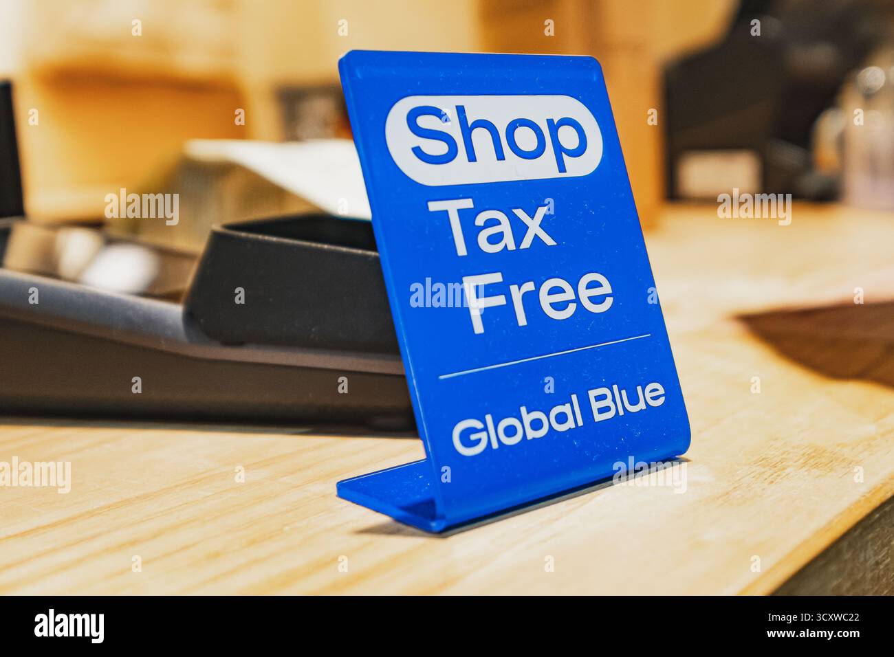 Un panneau bleu « Shop Tax Free » de Global Blue se trouve sur un comptoir en bois, avec un arrière-plan flou d'un cadre de magasin Banque D'Images