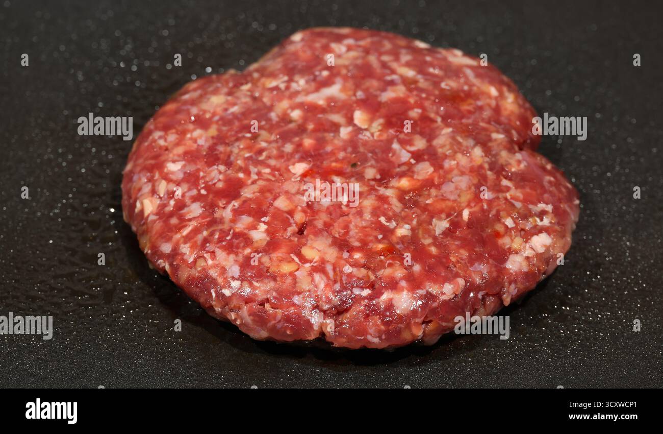 Patty hamburger cru juteux grésillant sur une poêle chaude et huileuse ou sur une surface de gril électrique, créant un arôme appétissant, promettant un h délicieux et satisfaisant Banque D'Images