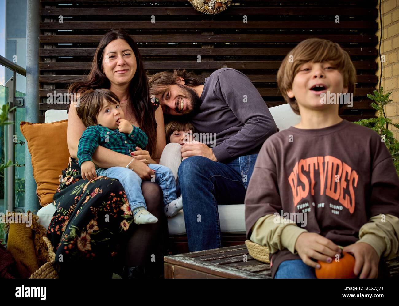 Une famille de cinq personnes se détend sur un patio rustique orné de citrouilles et d'un décor aux tons chaleureux, incarnant le charme de l'automne. La scène rayonne de confort Banque D'Images