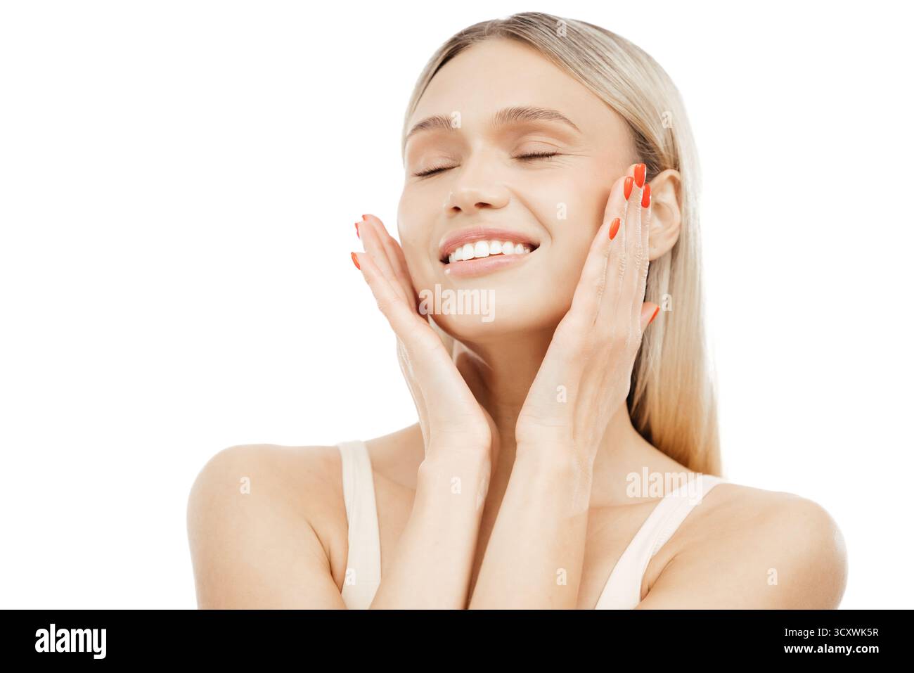 Une jeune femme à la peau claire sourit et touche son visage, soulignant sa routine beauté saine et l'importance des soins personnels et des soins de la peau Banque D'Images