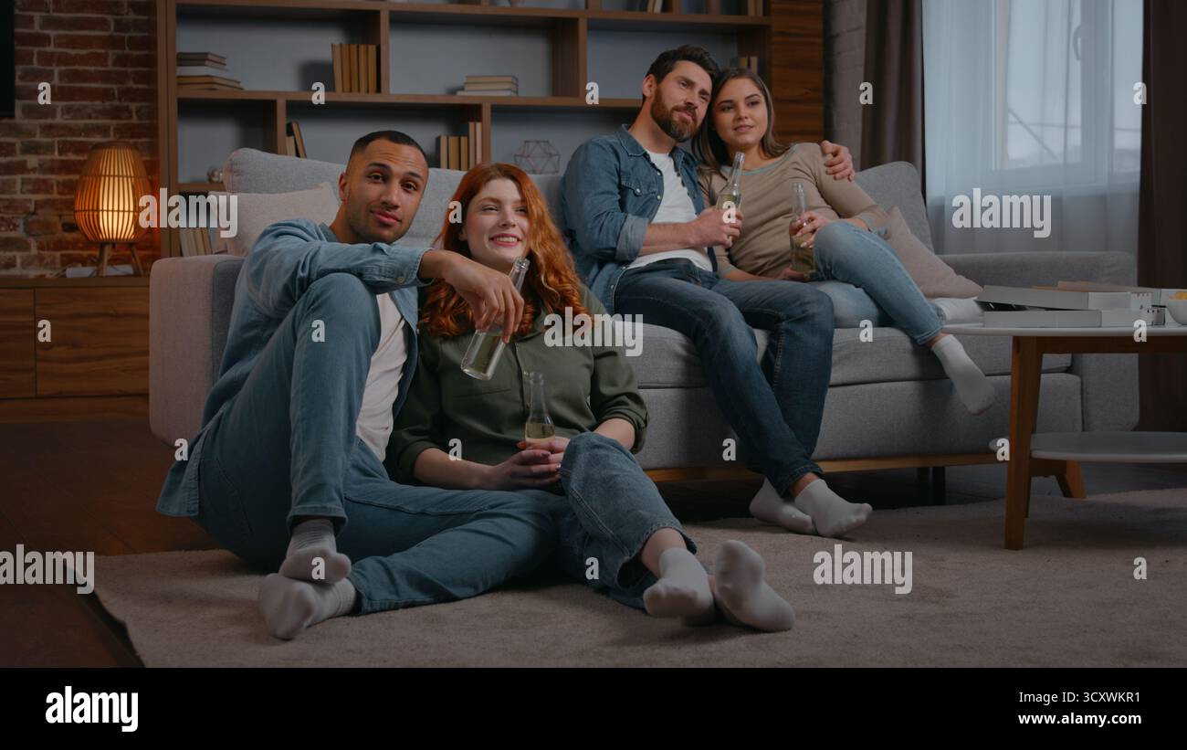 Deux couples mariés divers quatre amis multiraciaux regardant la télévision à la maison partie boire de la bière alcool cidre boisson dans le salon multiethnique Banque D'Images
