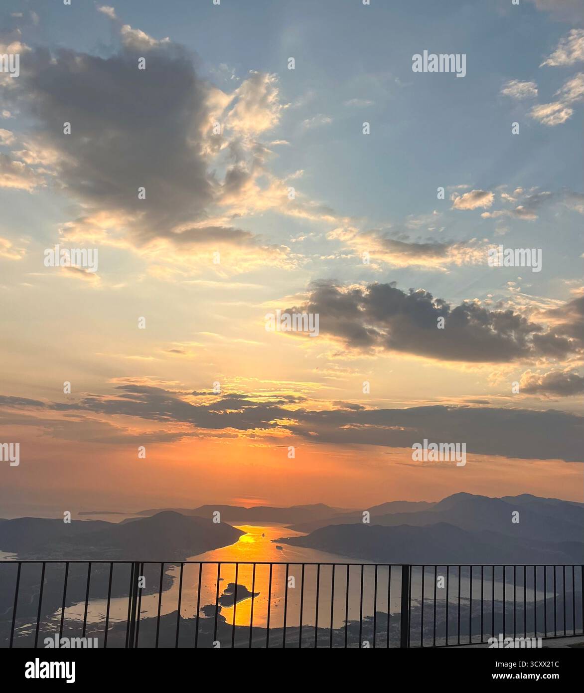 Vue imprenable sur le coucher du soleil sur la côte, avec la lumière dorée du soleil se reflétant sur la mer entre les silhouettes de montagne sous un ciel dramatique. - Image de stock capturée avec un smartphone