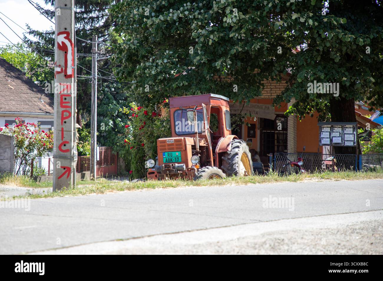 Vieux tracteur rouge IMT garé sur une route rurale sous un arbre dans le village de Vrdnik, Voïvodine, Serbie, par une journée d'été ensoleillée Banque D'Images