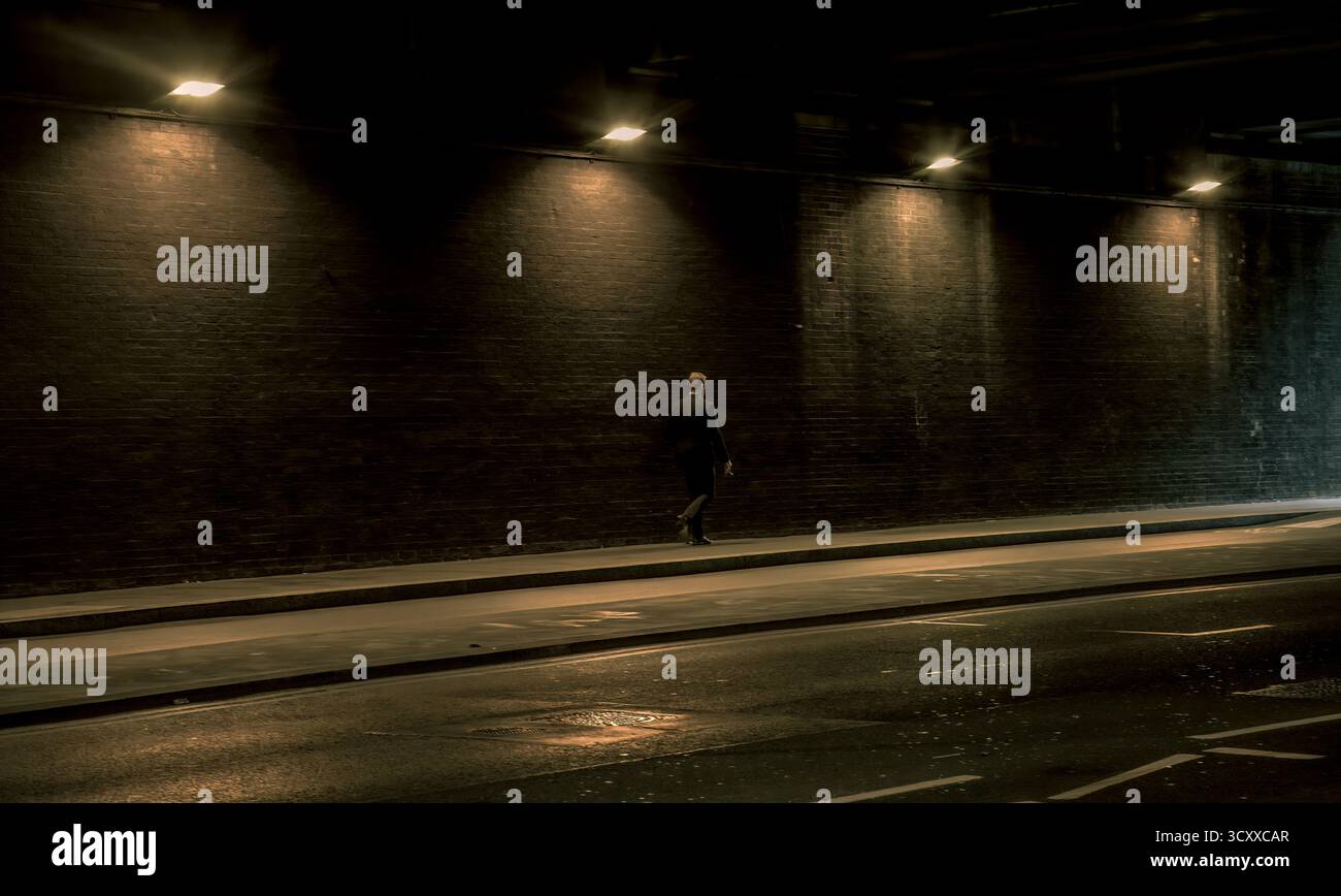 Homme marchant seul dans un tunnel faiblement éclairé la nuit. Banque D'Images