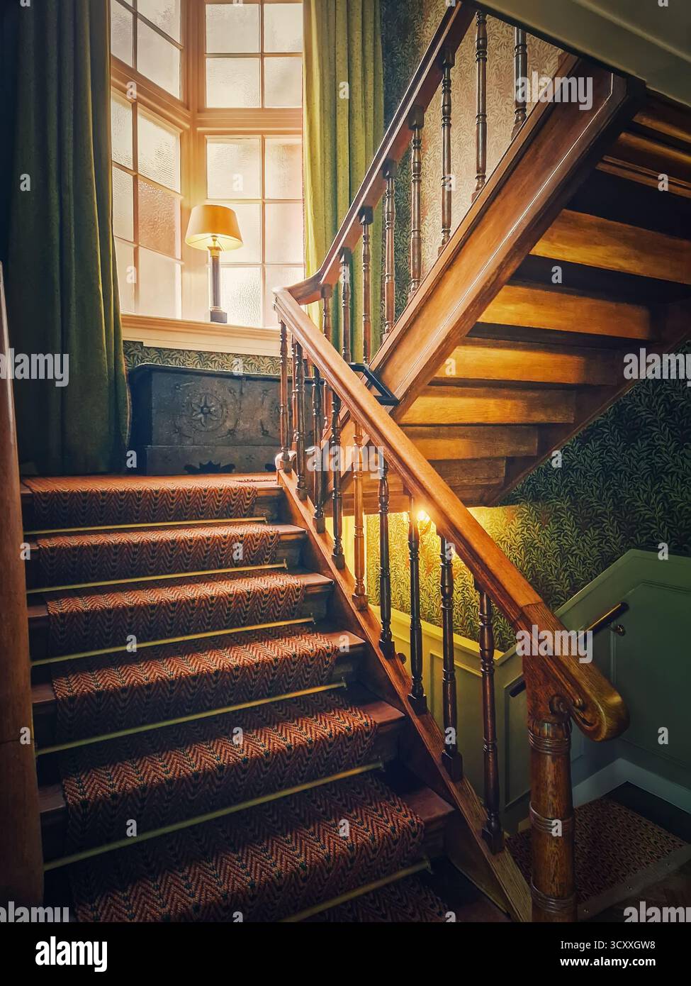 Un escalier en bois vintage avec des balustres classiques mène à une lumière douce qui filtre à travers la fenêtre. Ambiance chaleureuse et de mauvaise humeur, d'un vieil hôtel Banque D'Images
