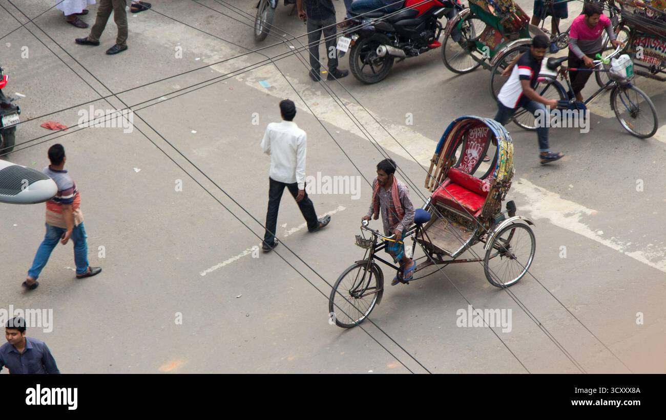 Transport traditionnel de pousse-pousse à Dhaka. Scène urbaine mettant en vedette un pousse-pousse à vélo. Piéton traversant la rue. Câbles au-dessus de la tête. Banque D'Images Transport traditionnel de pousse-pousse à Dhaka. Scène urbaine mettant en vedette un pousse-pousse à vélo. Piéton traversant la rue. Câbles au-dessus de la tête. Banque D'Images
