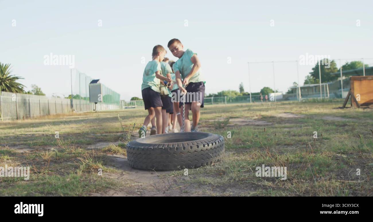 Six enfants en chemises vertes tirant des pneus de tracteur dans le champ, avec une chaîne lourde et une rampe en bois Banque D'Images