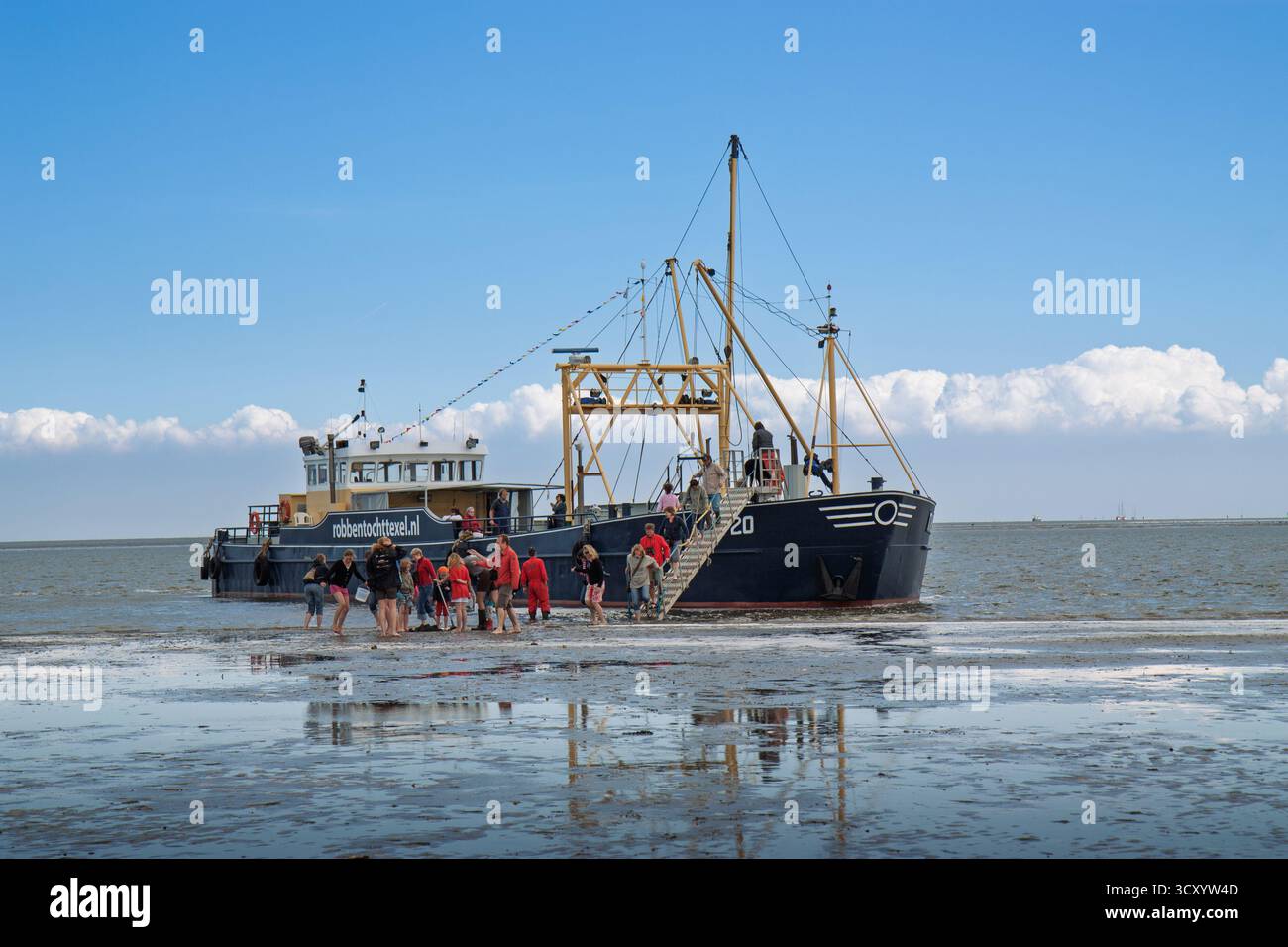 Un bateau d'observation des phoques est temporairement immobilisé sur les vasières de Texel, les passagers débarquant pour marcher sur la zone de marée exposée. Banque D'Images