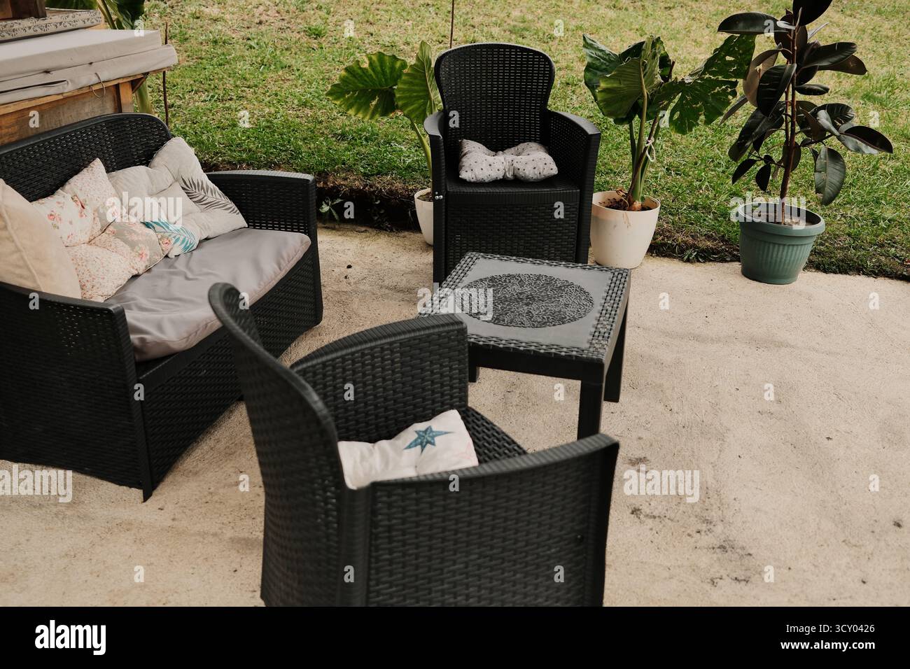 Coin salon extérieur confortable avec mobilier en osier noir, oreillers et plantes en pot. Idéal pour la maison, la détente et les concepts de décoration de jardin. Banque D'Images