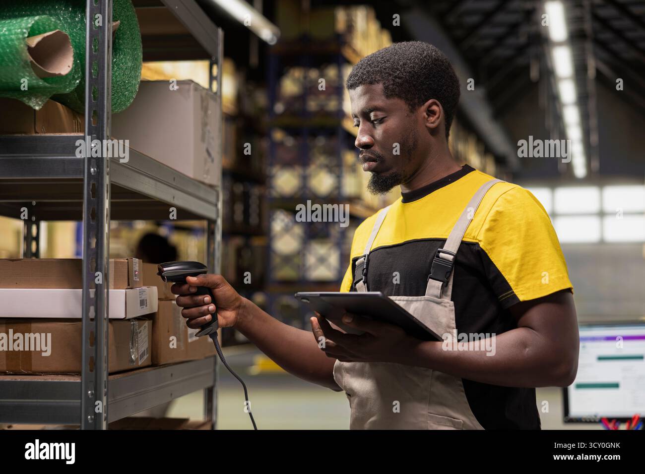 Travailleur masculin d'entrepôt scannant les numéros d'information de suivi sur les étiquettes de codes-barres, enregistrant les étiquettes d'expédition sur les boîtes en carton. Le personnel du centre de distribution indique l'état du colis et l'itinéraire de livraison. Banque D'Images