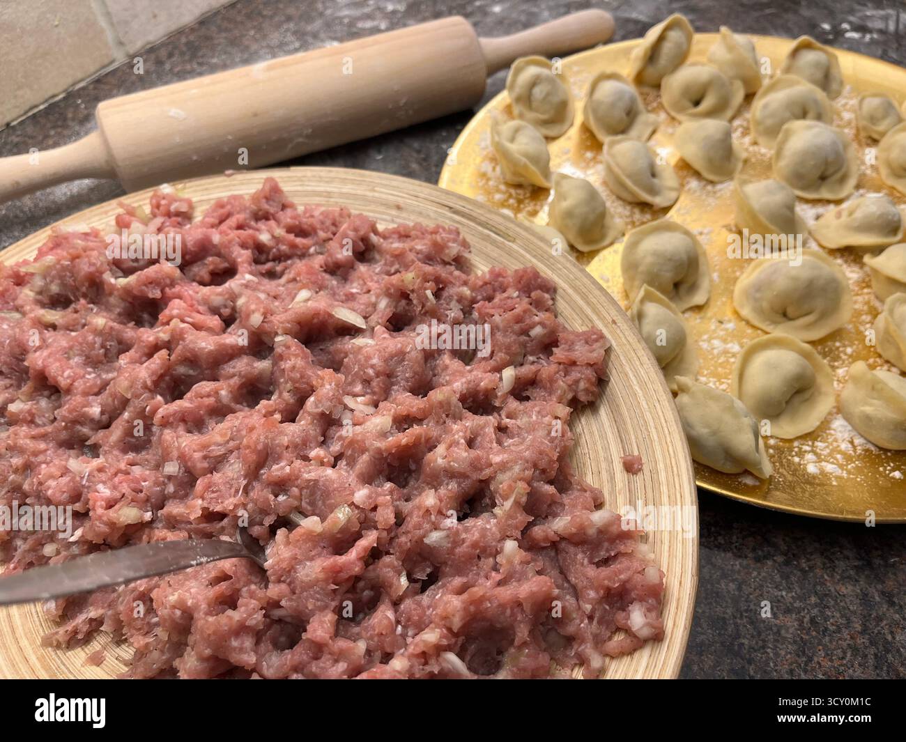 Boulettes maison non cuites sur la plaque dorée, viande hachée sur la plaque de bambou et un rouleau à pâtisserie sur la table noire dans la cuisine. - Image de stock capturée avec un smartphone