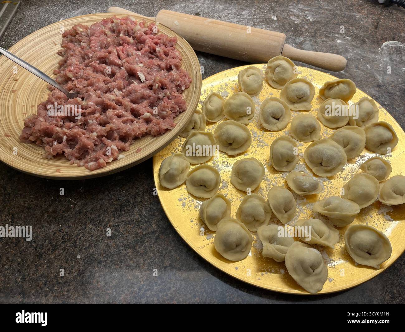 Boulettes maison non cuites sur la plaque dorée, viande hachée sur la plaque de bambou et un rouleau à pâtisserie sur la table noire dans la cuisine. - Image de stock capturée avec un smartphone