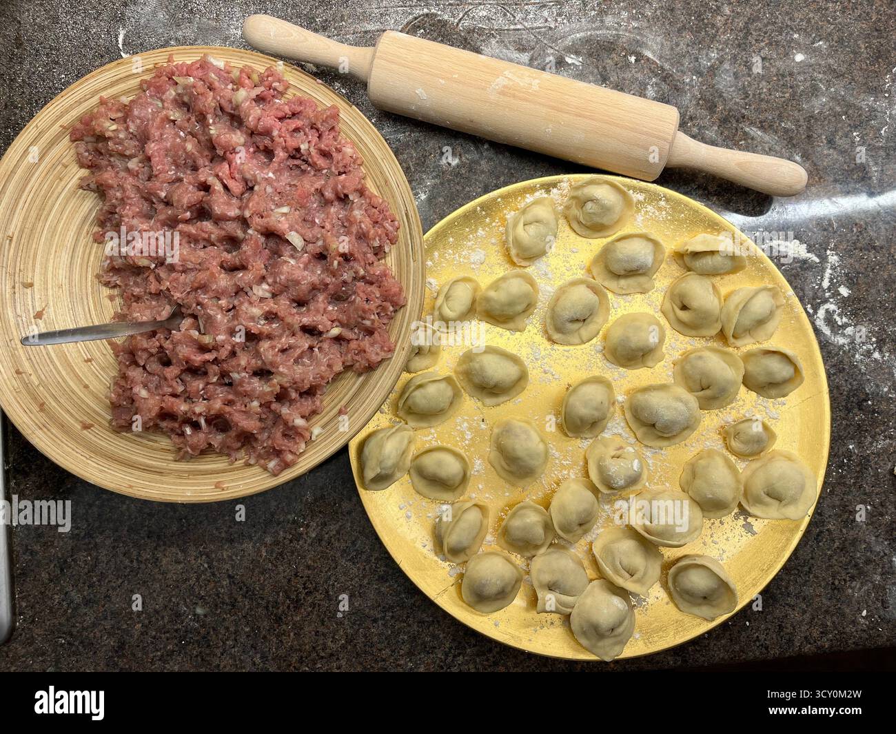 Boulettes maison non cuites sur la plaque dorée, viande hachée sur la plaque de bambou et un rouleau à pâtisserie sur la table noire dans la cuisine. - Image de stock capturée avec un smartphone