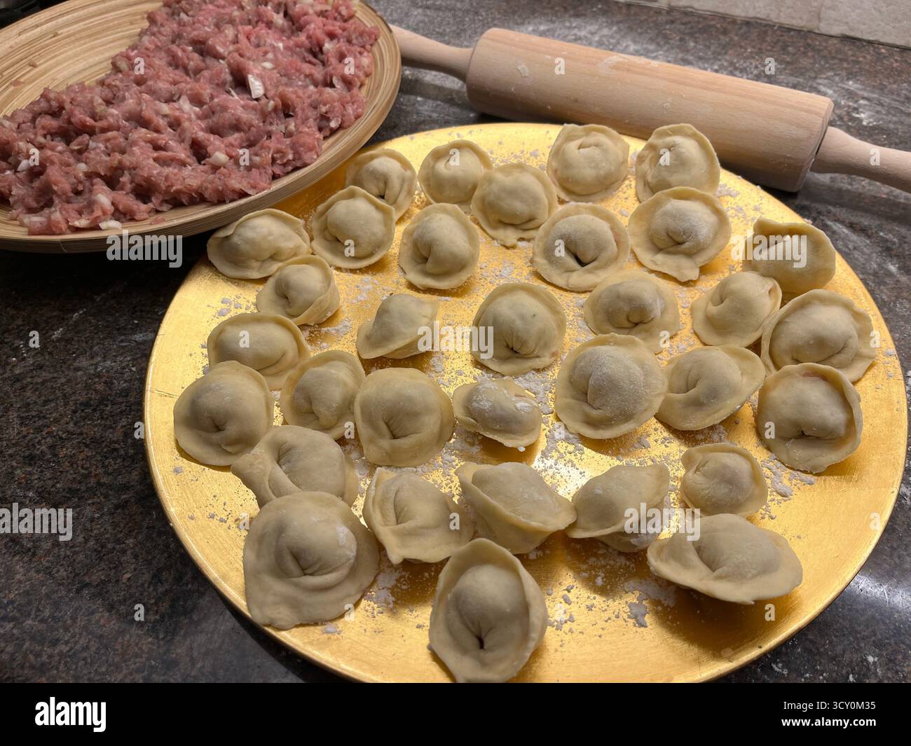 Boulettes maison non cuites sur la plaque dorée, viande hachée sur la plaque de bambou et un rouleau à pâtisserie sur la table noire dans la cuisine. - Image de stock capturée avec un smartphone