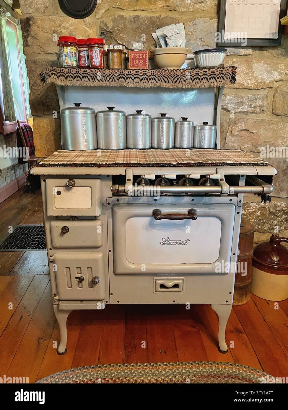 Scène de cuisine vintage avec un poêle blanc antique, des boîtes en métal et des articles de garde-manger rustiques contre un fond de mur de pierre - Image de stock capturée avec un smartphone