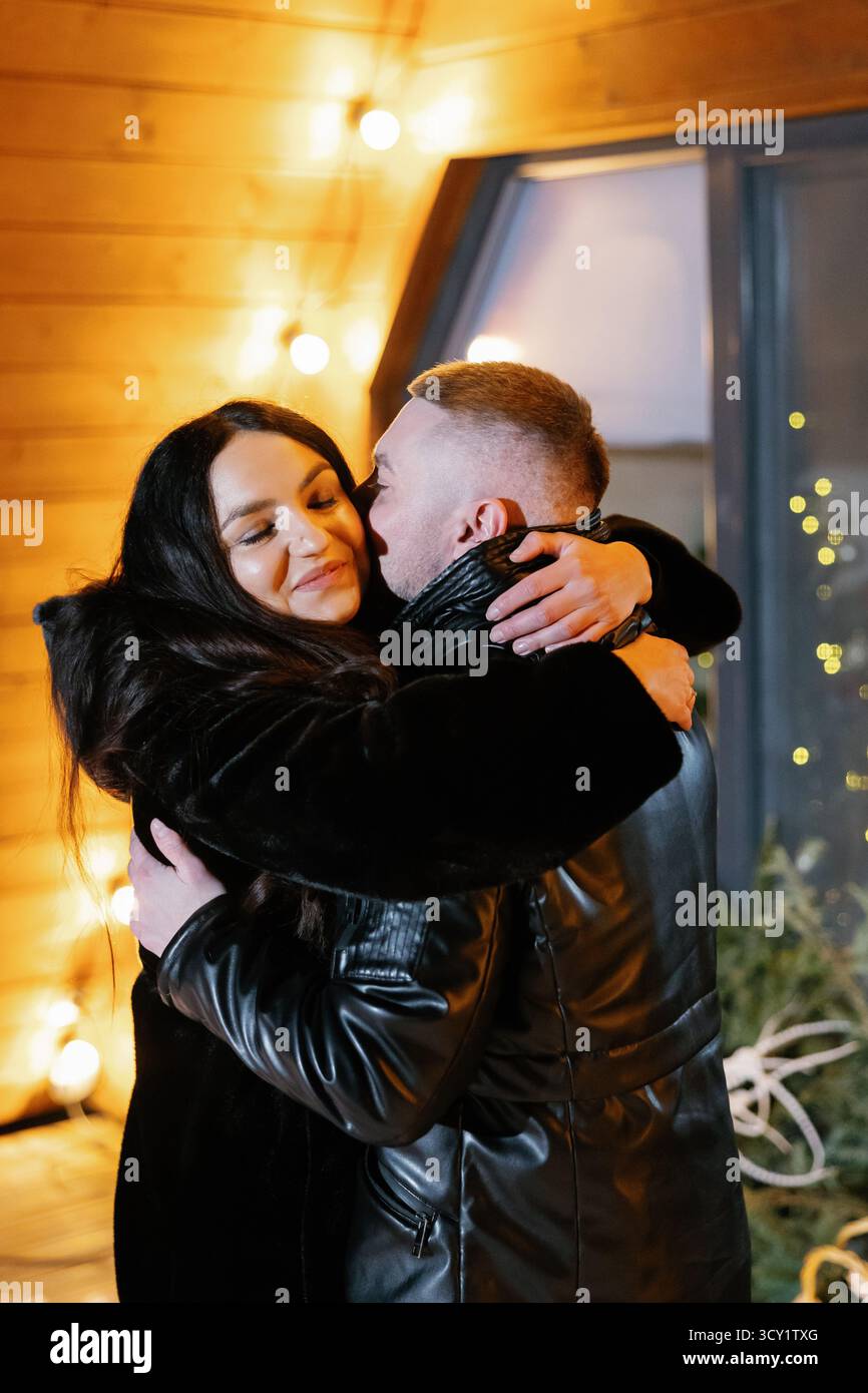 Homme et femme embrassant tendrement à l'extérieur le soir d'hiver devant leur maison décorée Banque D'Images