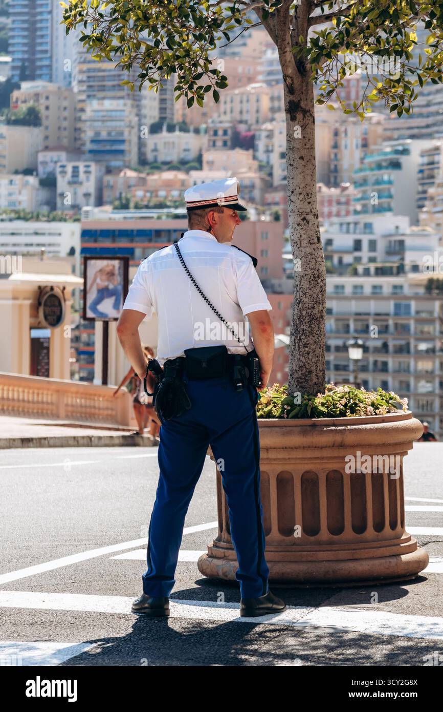 Monte Carlo, Monaco - 28 juin 2025 : policier debout près de la place du Casino surplombant les bâtiments de la ville et la lumière méditerranéenne Banque D'Images