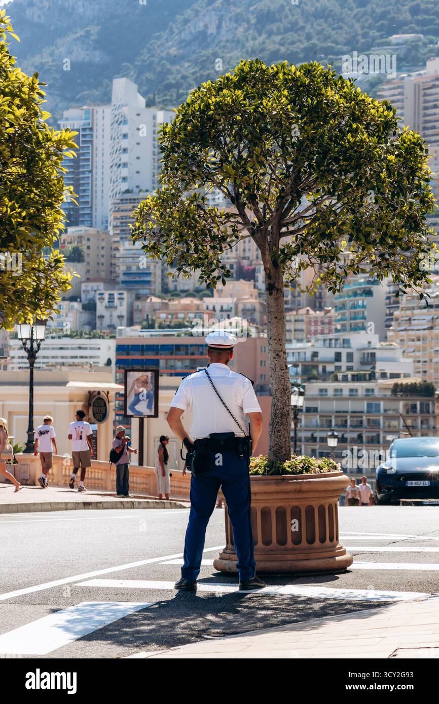 Monte Carlo, Monaco - 28 juin 2025 : policier debout près de la place du Casino surplombant les bâtiments de la ville et la lumière méditerranéenne Banque D'Images