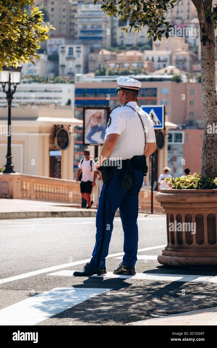 Monte Carlo, Monaco - 28 juin 2025 : policier debout près de la place du Casino surplombant les bâtiments de la ville et la lumière méditerranéenne Banque D'Images