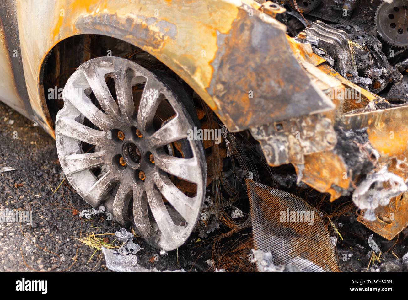 Un véhicule brûlé se trouve dans un emplacement vide, avec une roue endommagée et un extérieur carbonisé visible. Des débris dispersés et des restes du feu entourent le W. Banque D'Images