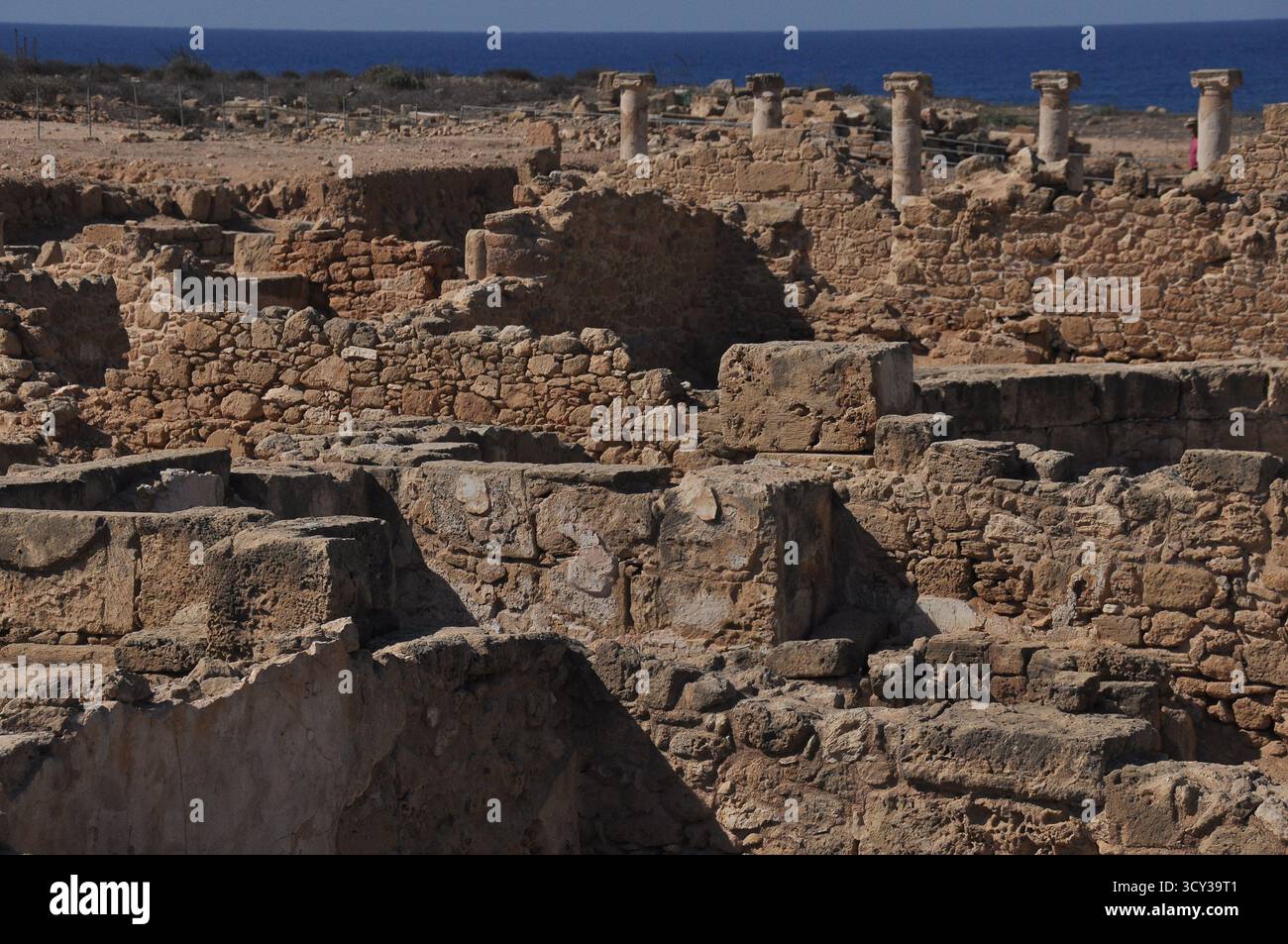 Les ruines de pierre d'une civilisation ancienne sont dispersées à travers un paysage côtier sous un soleil éclatant, surplombant la mer bleue calme. Les piliers se dressent Banque D'Images