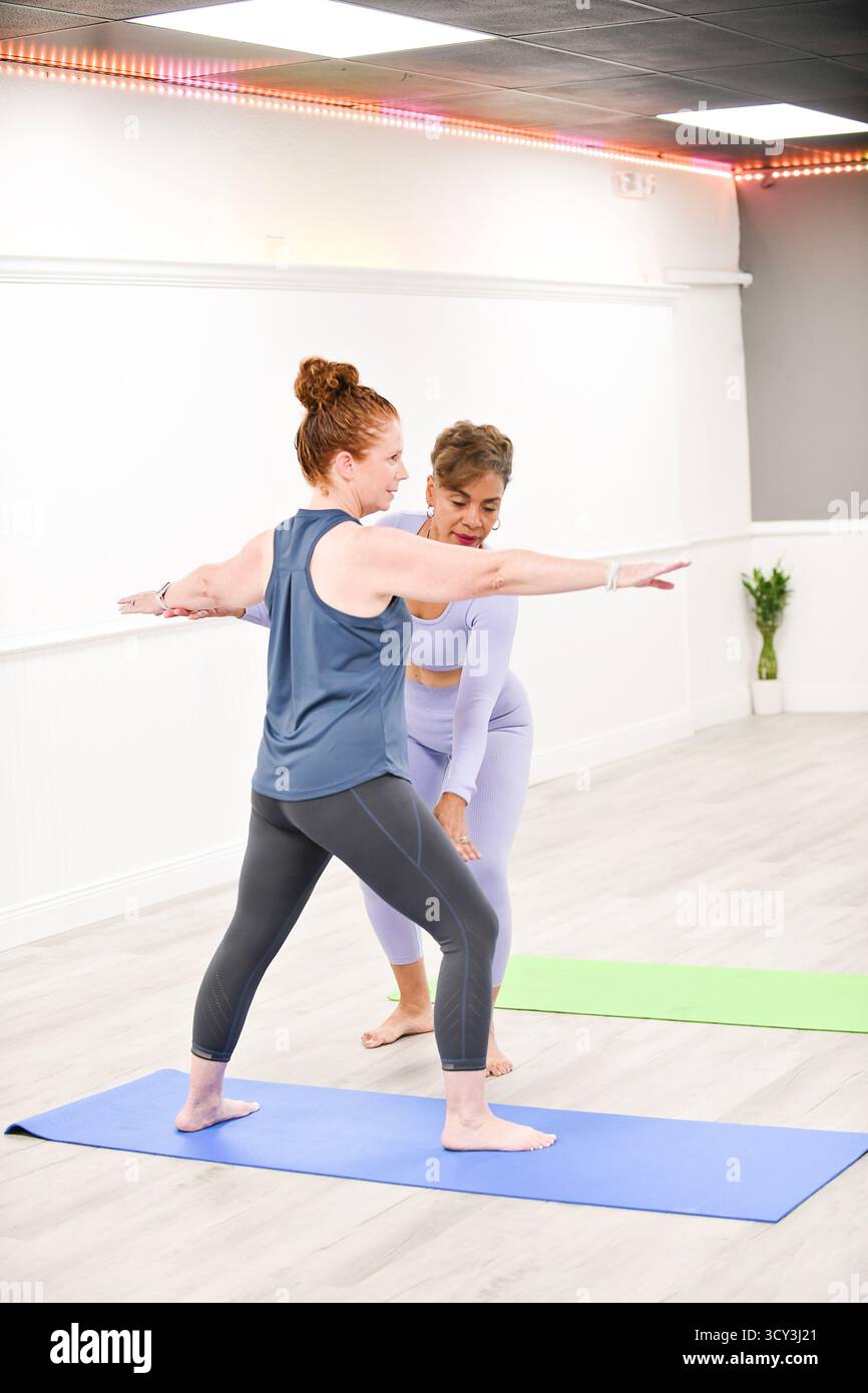 Instructeur de yoga guidant l'étudiant en guerrier II pose sur tapis. Banque D'Images