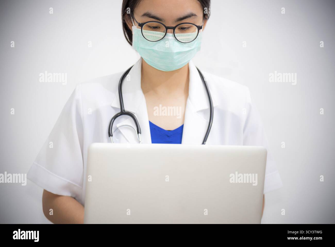 Studio portrait une jeune femme asiatique porte des lunettes et masque à la sécurité Coronavirus regardant l'ordinateur portable, le médecin avec stéthoscope travaille sur Banque D'Images