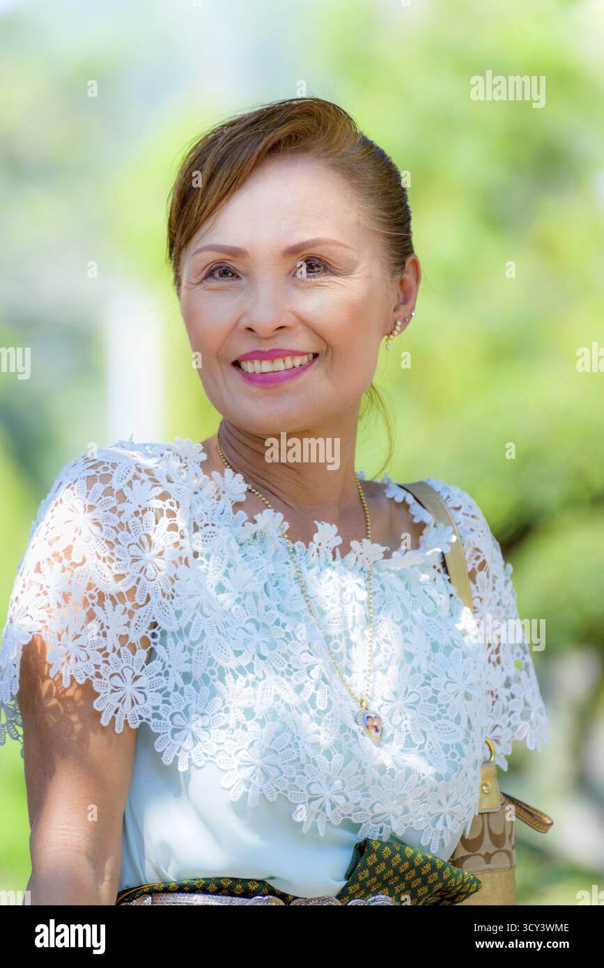 Portrait avant de la belle femme asiatique d'âge moyen en bonne santé, robe dans le style thaïlandais des vêtements souriant joyeusement sur le fond vert de l'arbre de la nature Banque D'Images