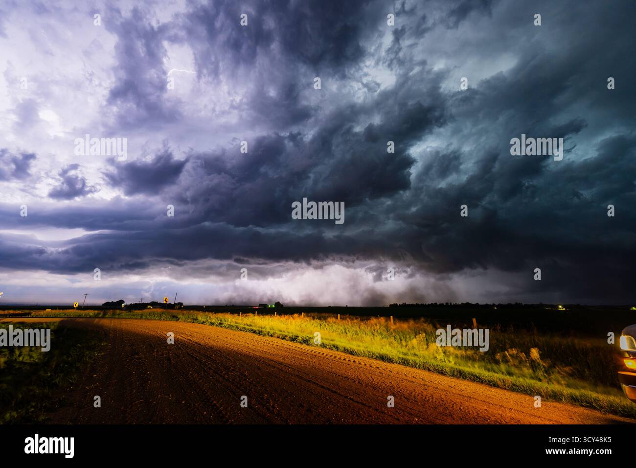 Un éclair lumineux clignote dans un nuage d'orage sombre au-dessus d'une route de campagne, éclairant un ciel dramatique rempli d'ombre, de texture et d'atmosphère sombre Banque D'Images