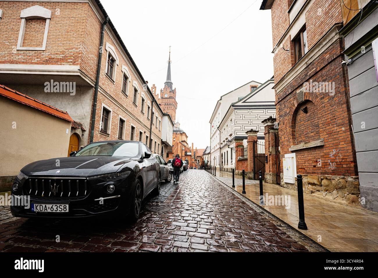 Tarnow, Pologne - 10 octobre 2025 : une élégante Maserati Levante noire garée le long d'une rue pavée humide à Tarnow près d'immeubles en briques. Banque D'Images