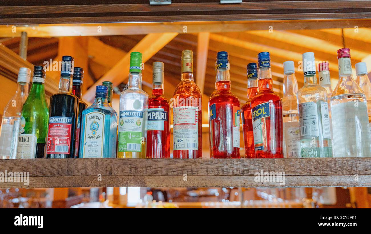 08.23.25 Oberaula, Allemagne, Une collection variée de bouteilles de liqueur est soigneusement disposée sur une étagère en bois. La variété de couleurs et d'étiquettes met en évidence Banque D'Images