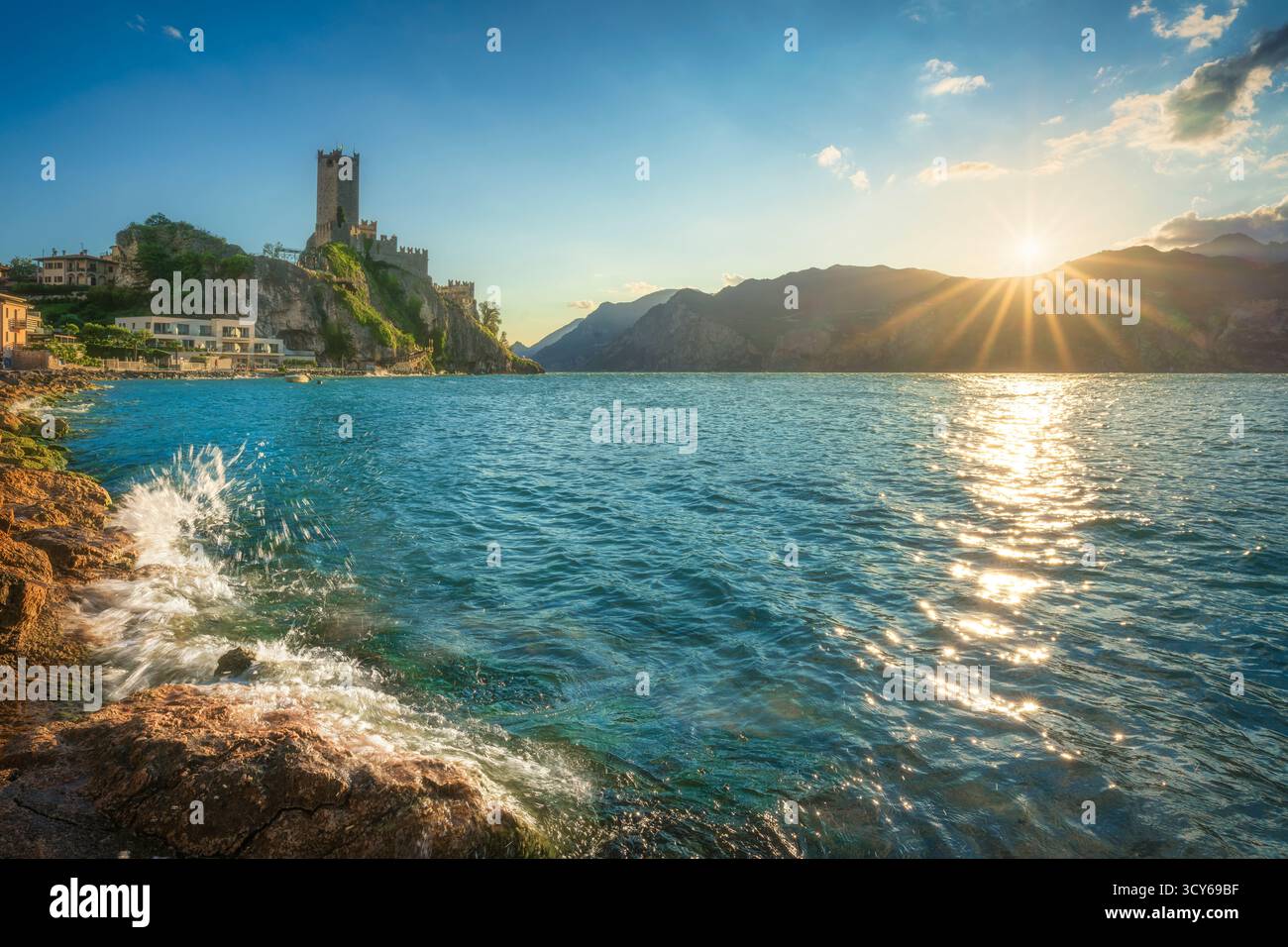 Spectaculaire coucher de soleil sur le château de Scaliger à Malcesine, lac de Garde. Sunburst sur les montagnes et lumière étincelante sur les vagues et les rochers dans la for Banque D'Images Spectaculaire coucher de soleil sur le château de Scaliger à Malcesine, lac de Garde. Sunburst sur les montagnes et lumière étincelante sur les vagues et les rochers dans la for Banque D'Images