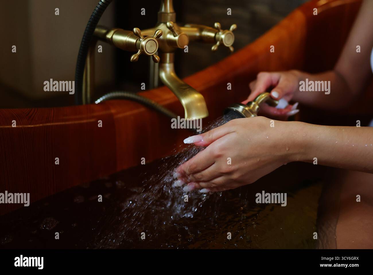 Eau chaude coulant sur les mains dans l'élégante baignoire en bois, détente et détail spa Banque D'Images
