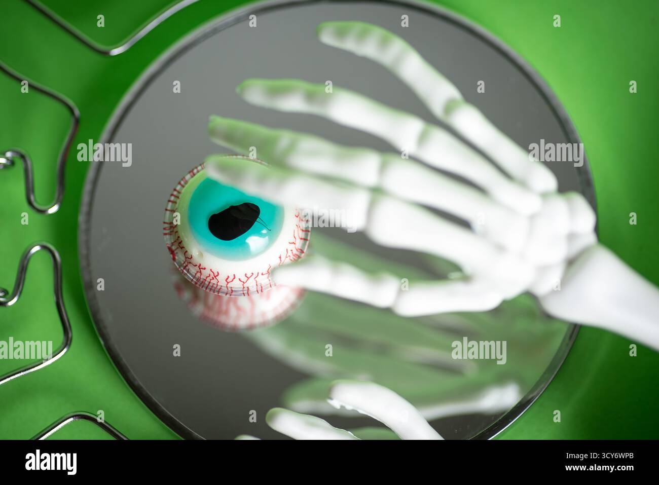 Une scène illustrative mettant en scène la main d'un squelette qui tend délicatement vers un œil réaliste, représentant de manière éclatante des vaisseaux sanguins complexes contre une lumière vive Banque D'Images