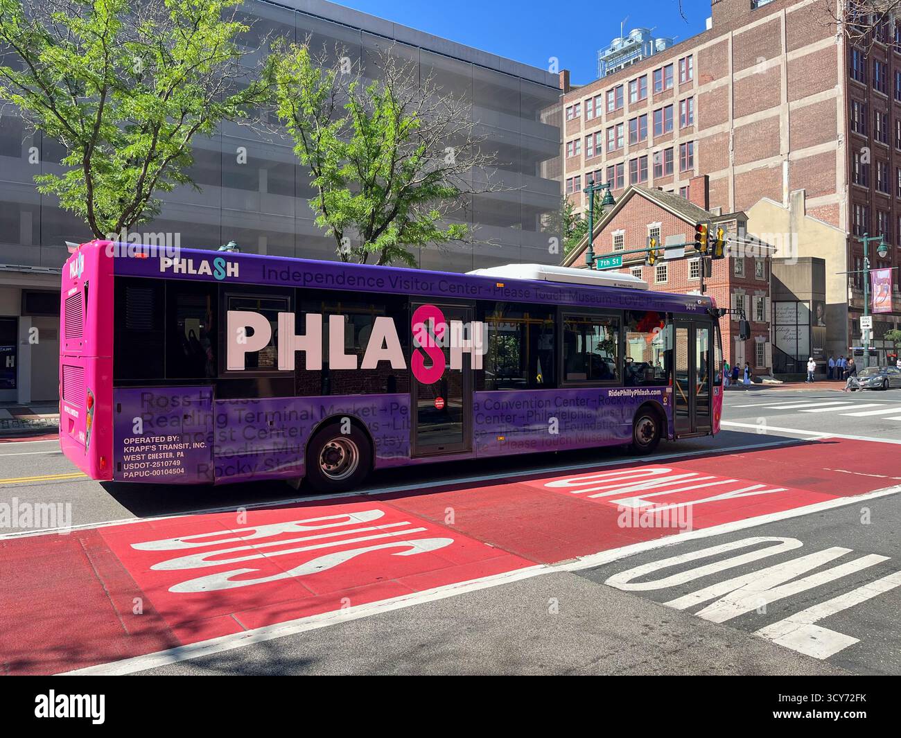 Un bus Phlash violet avec le mot Philly dessus. Le bus descend une rue. Il y a quelques personnes sur le trottoir Banque D'Images Un bus Phlash violet avec le mot Philly dessus. Le bus descend une rue. Il y a quelques personnes sur le trottoir Banque D'Images