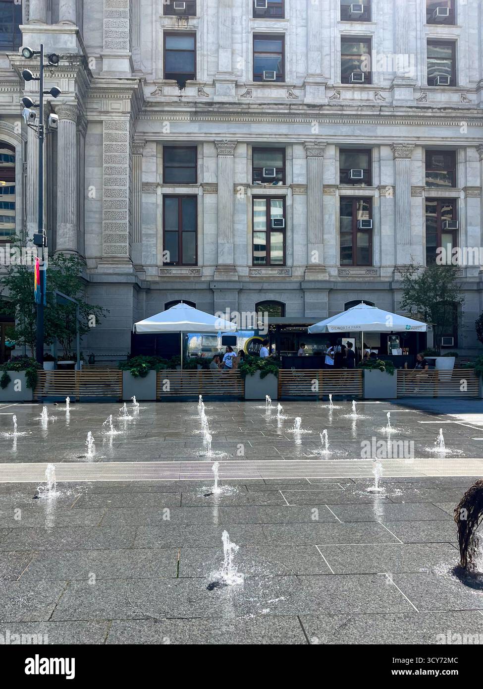 Un grand bâtiment avec une fontaine devant lui. La fontaine a plusieurs petites fontaines et est entourée de parasols Banque D'Images Un grand bâtiment avec une fontaine devant lui. La fontaine a plusieurs petites fontaines et est entourée de parasols Banque D'Images