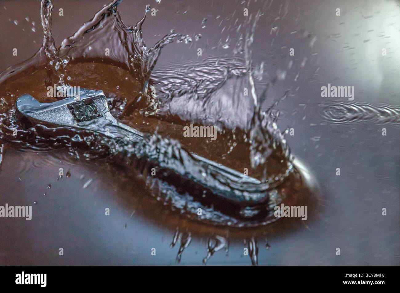 Clé métallique réglable partiellement immergée dans l'eau, entourée d'arcs d'éclaboussure et de gouttelettes. La capture ultra-rapide accentue les mouvements. Banque D'Images