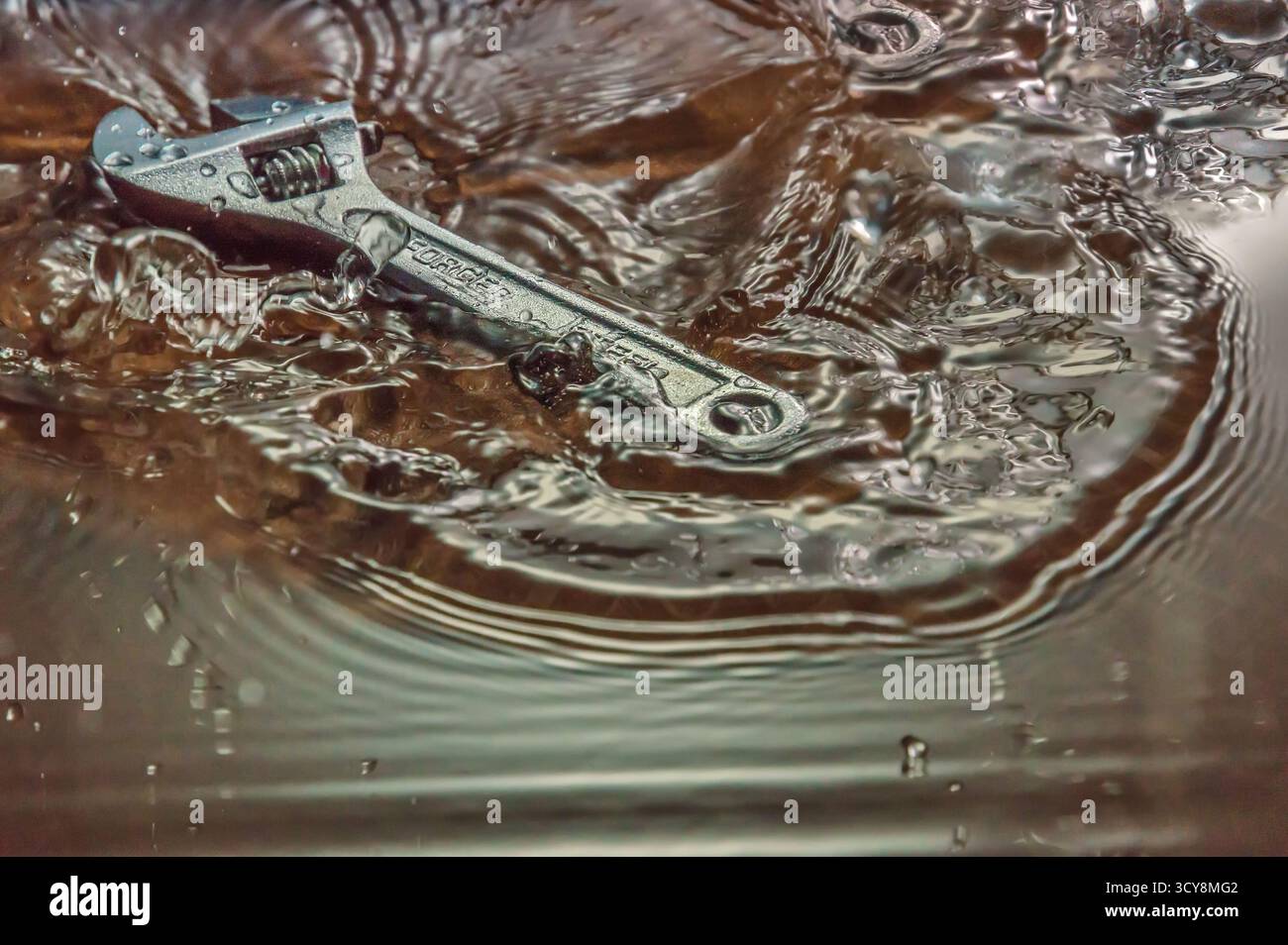 Clé métallique étiquetée « DROP FORGED » partiellement immergée dans l’eau. Banque D'Images