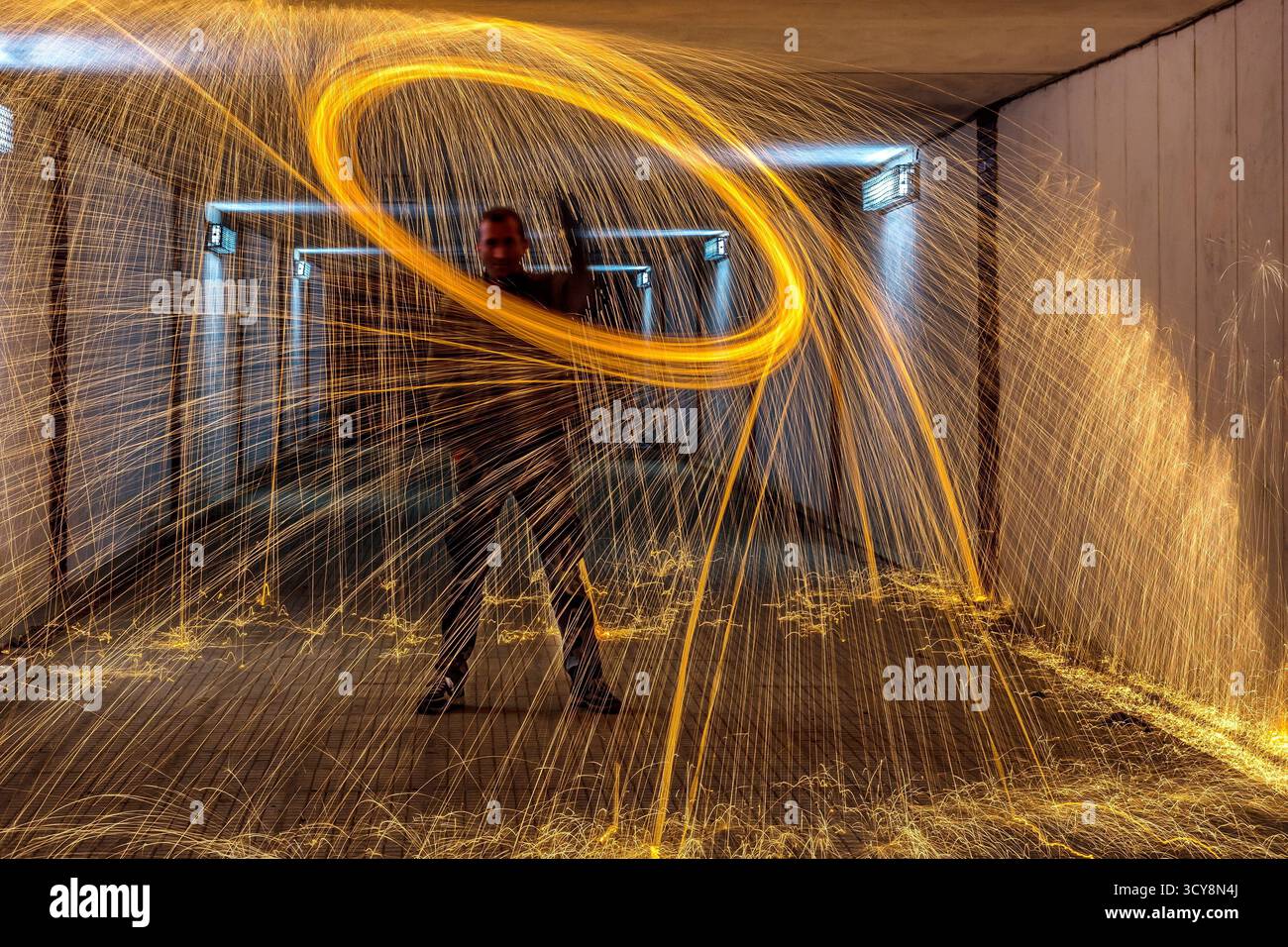 La laine d'acier filant dans le tunnel crée un anneau vif d'étincelles. L'exposition longue capture le mouvement et le contraste avec des lumières bleues. Banque D'Images