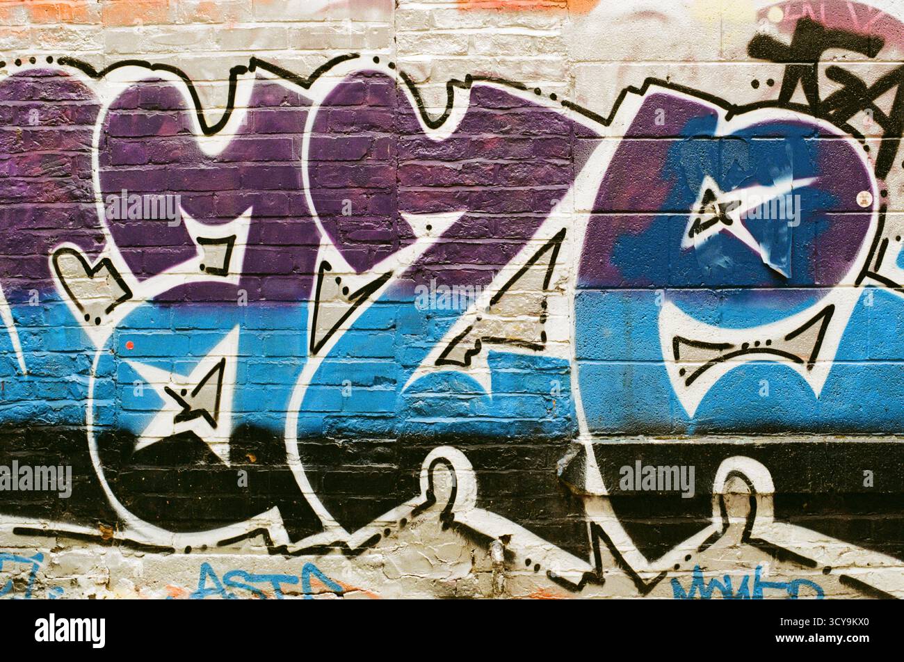 Graffiti violet et bleu sur un mur de briques à Manchester, en Angleterre, photographié sur un film couleur Fujifilm 200, montrant des détails audacieux du Street art urbain Banque D'Images
