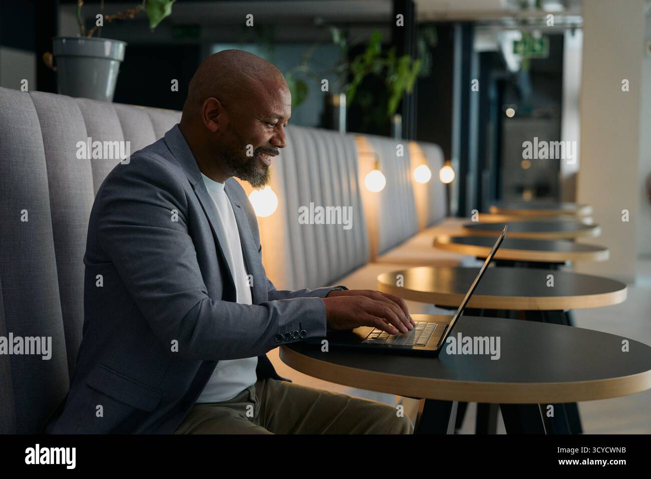 Vue latérale de l'homme d'affaires mûr souriant dans le travail décontracté intelligent sur ordinateur portable dans le salon de bureau Banque D'Images