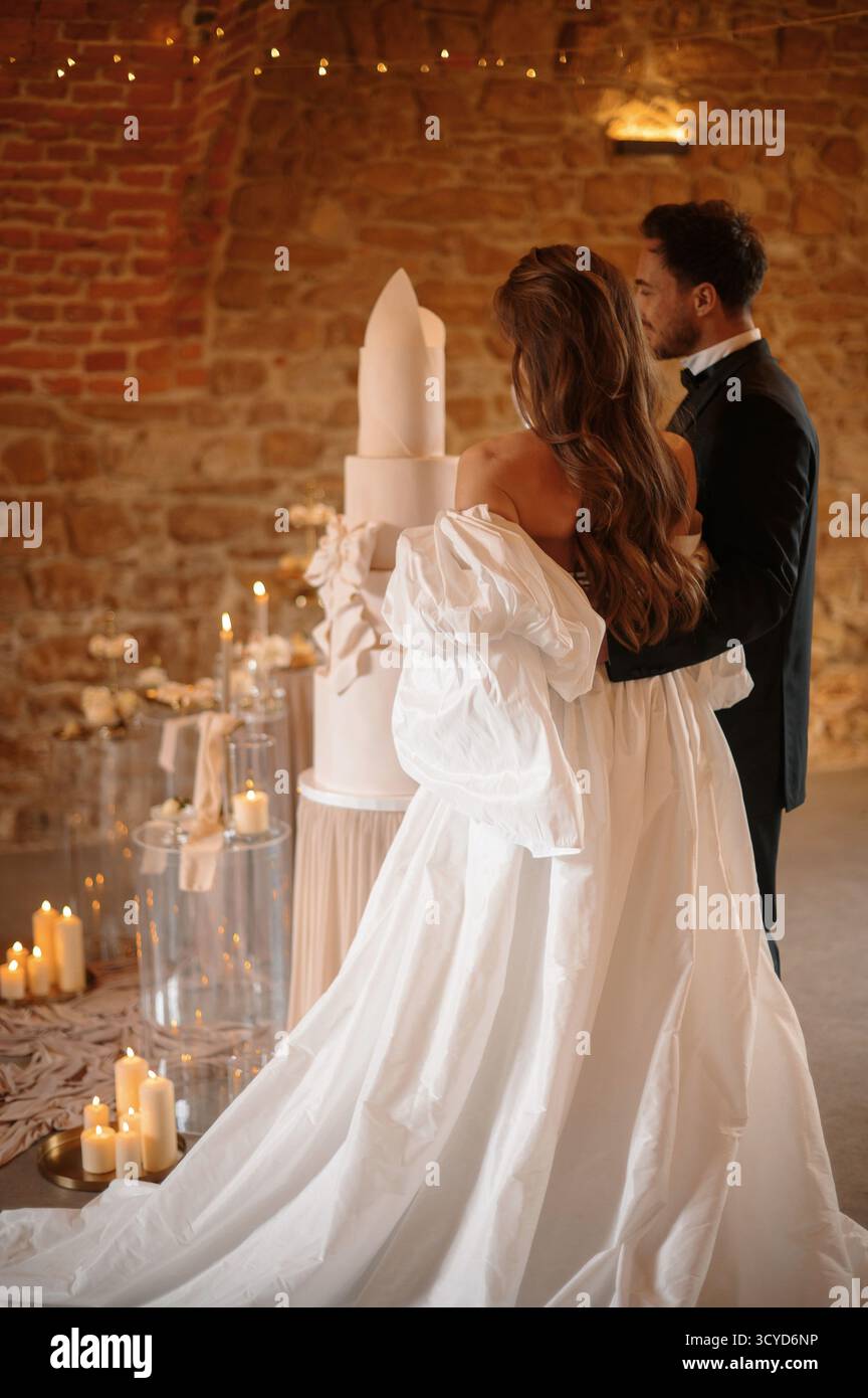 Mariée et mariée debout par un grand gâteau de mariage dans un cadre rustique. Banque D'Images