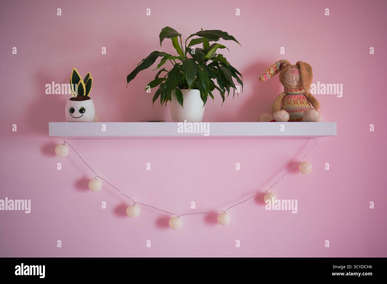 Étagère rose Cozy Nursery décorée avec des plantes en pot ludiques, un jouet de lapin en peluche, et des lumières suspendues à cordes de boules de coton pour la salle d'enfant fantaisiste Ambi Banque D'Images