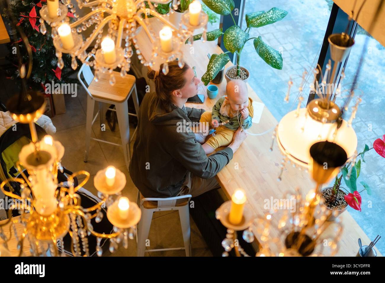 Homme avec un enfant en bas âge dans les bras assis dans le café. La vue aérienne capture la relation père-bébé, la responsabilité parentale, l'amour de la famille et l'atmosphère chaleureuse dans le restaurant public. Banque D'Images