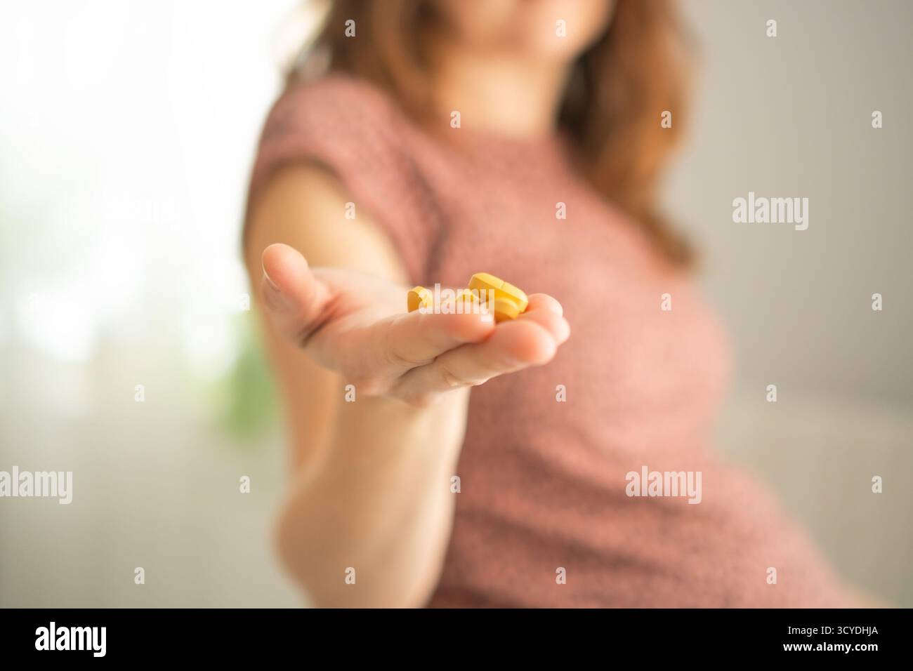 Gros plan de la main de la mère qui tient le comprimé prescrit alors que l'autre main protège son ventre. Soins prudents pendant la grossesse. Banque D'Images