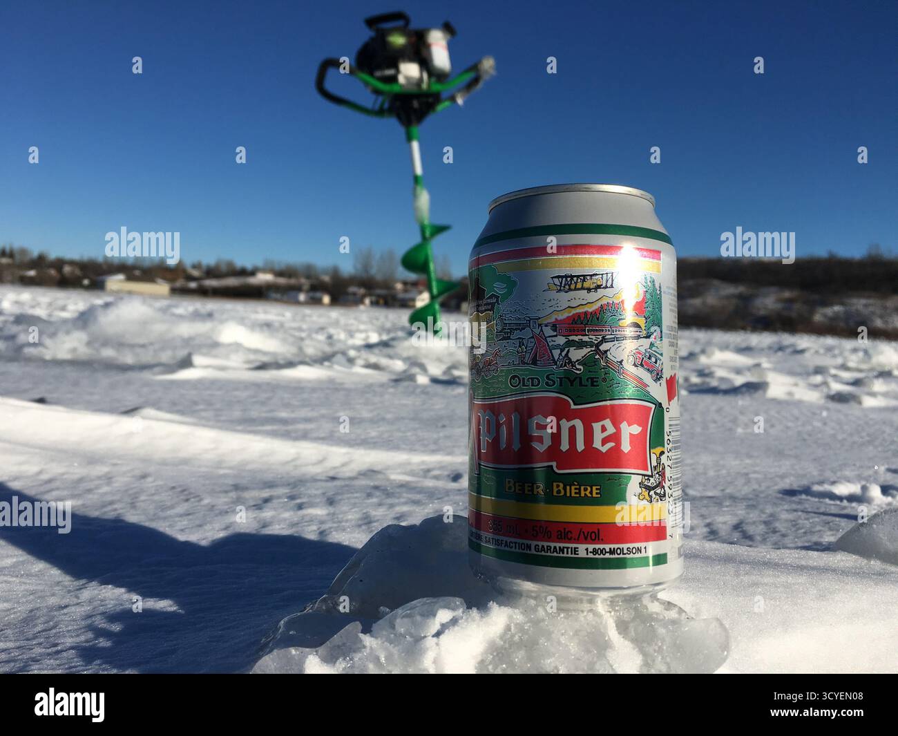 Configuration de pêche sur glace sur un lac enneigé avec une boîte de Pilsner Old style, sous un ciel bleu clair, mêlant sport d'hiver et détente. Banque D'Images